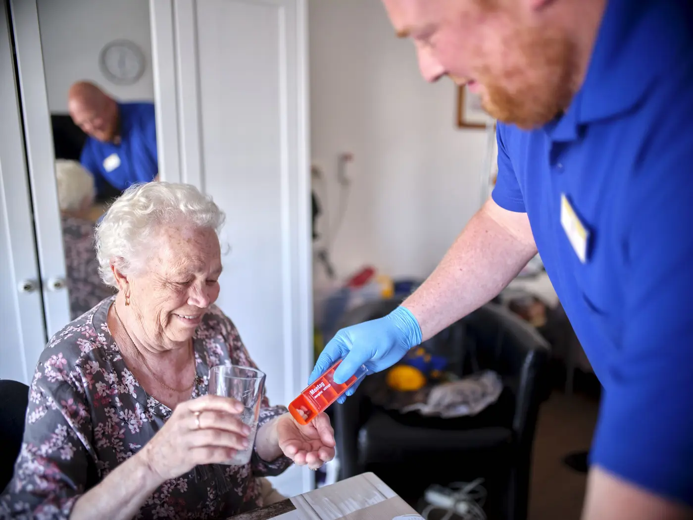 Ein Mitarbeiter übergibt einer Seniorin ihre Medikamente.