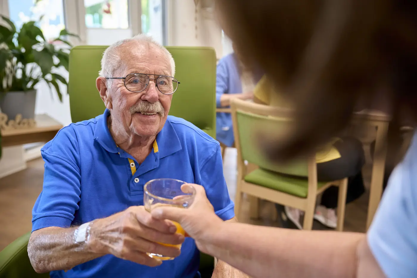 Ein Mitarbeiter reicht einem Senioren ein Glas.